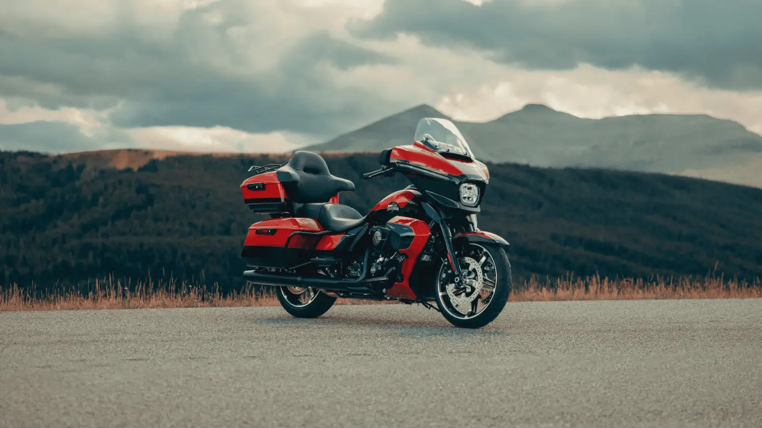 A vibrant red motorcycle, the 2025 Harley-Davidson® Street Glide® Ultra, rests on a road with stunning mountains behind it.