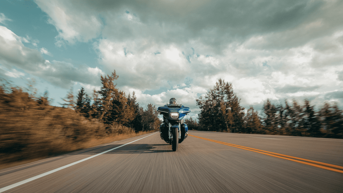 Rider cruising on a 2025 Harley-Davidson® Street Glide® Ultra down an open road, spotlighting its full touring setup, aerodynamic design, and long-distance performance.