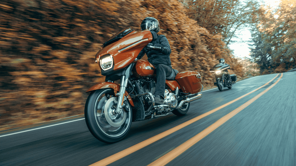 2025 Harley-Davidson® Street Glide® in vibrant orange color leading on a scenic Sanford, FL road with another bike in the distance.