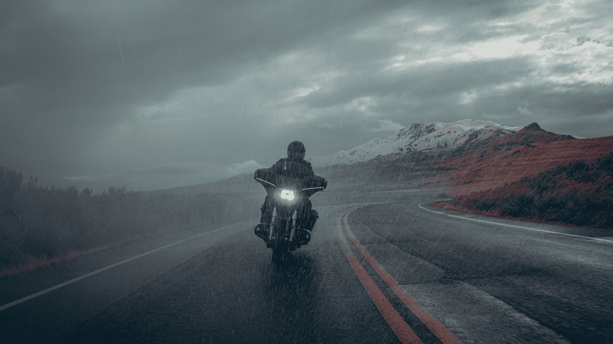 Rider on a 2025 Harley-Davidson® Street Glide® powering through a rain-soaked mountain road, highlighting its LED headlamp and touring silhouette.