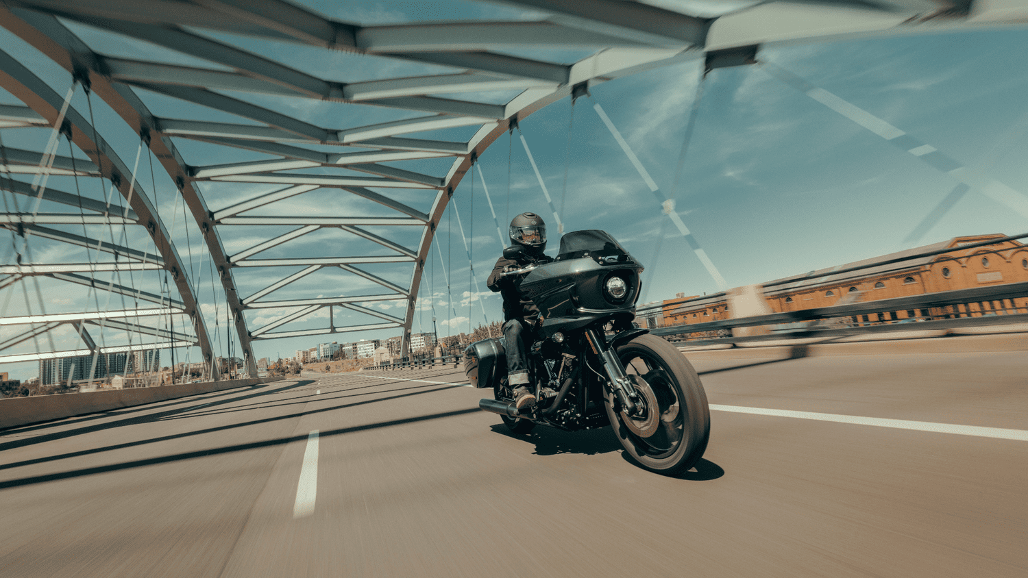 Rider cruising across a modern bridge on the 2025 Harley-Davidson® Low Rider® ST, showcasing its LED lighting near Sanford, FL.