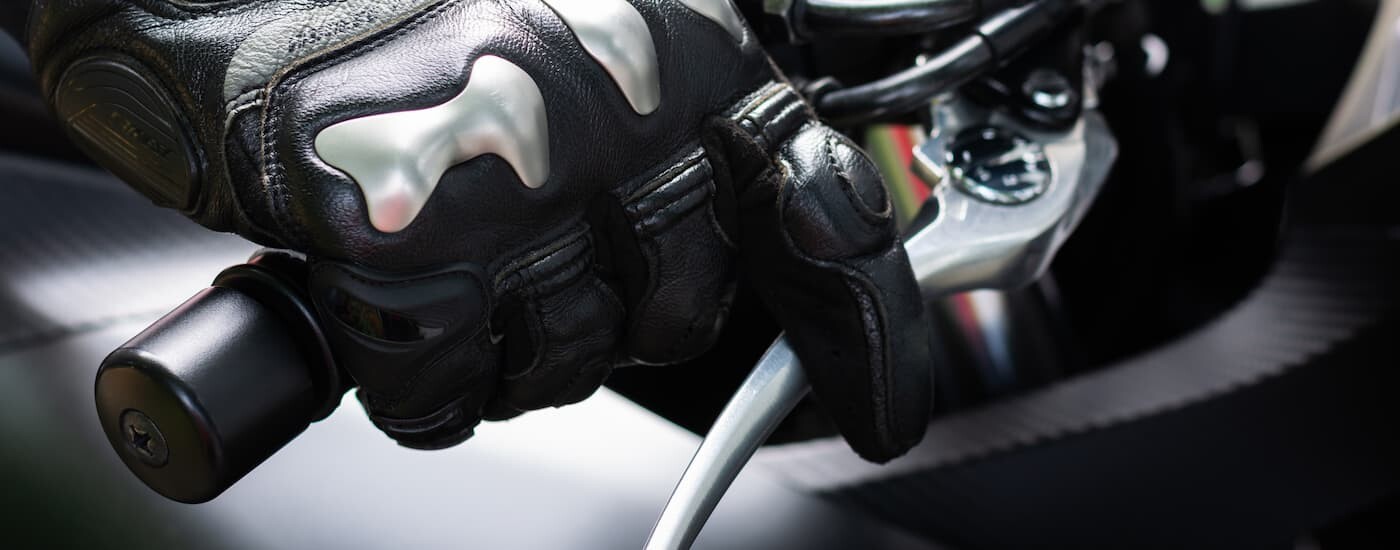 A close up of a gloved hand on a motorcycle throttle is shown.