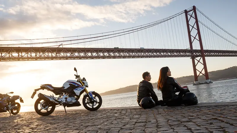 Two people sat near a suspension bridge with their BMW motorcycle