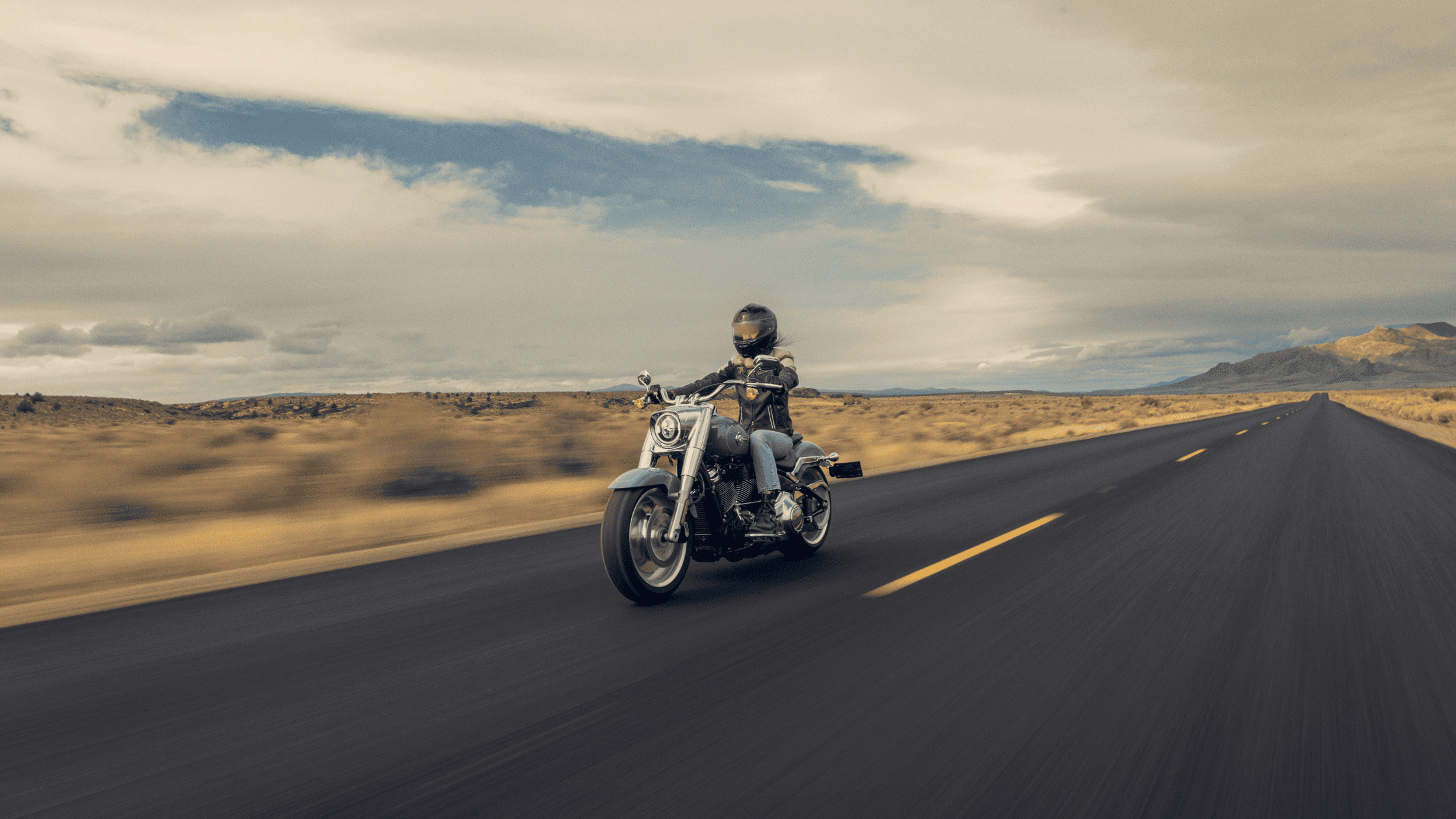 Motorcyclist riding a Harley-Davidson Fat Boy 114 on an open road.