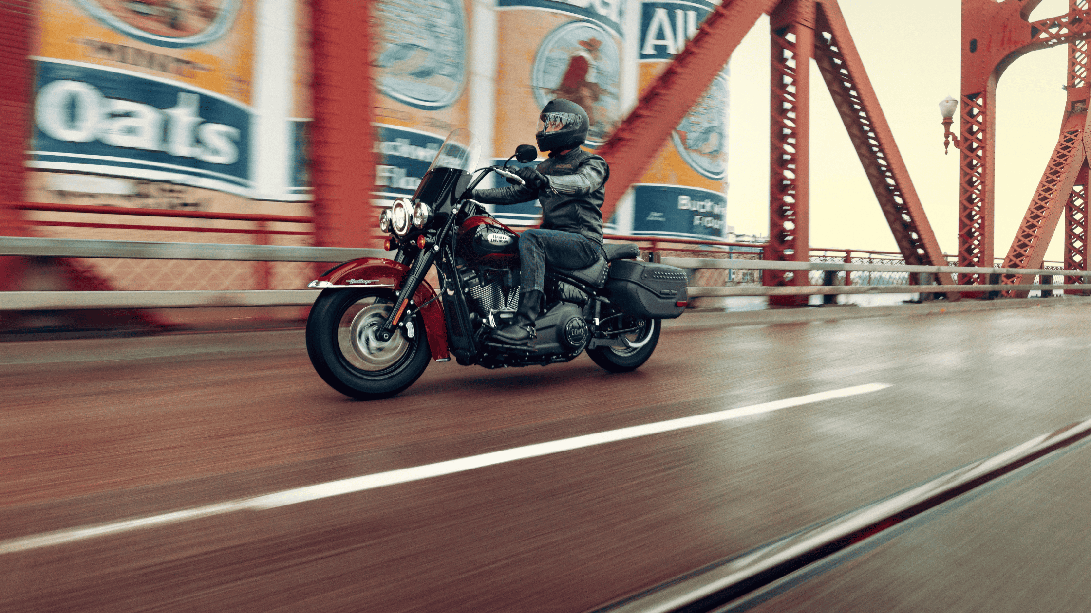 Motorcyclist riding a Harley-Davidson Heritage Classic on a red bridge.