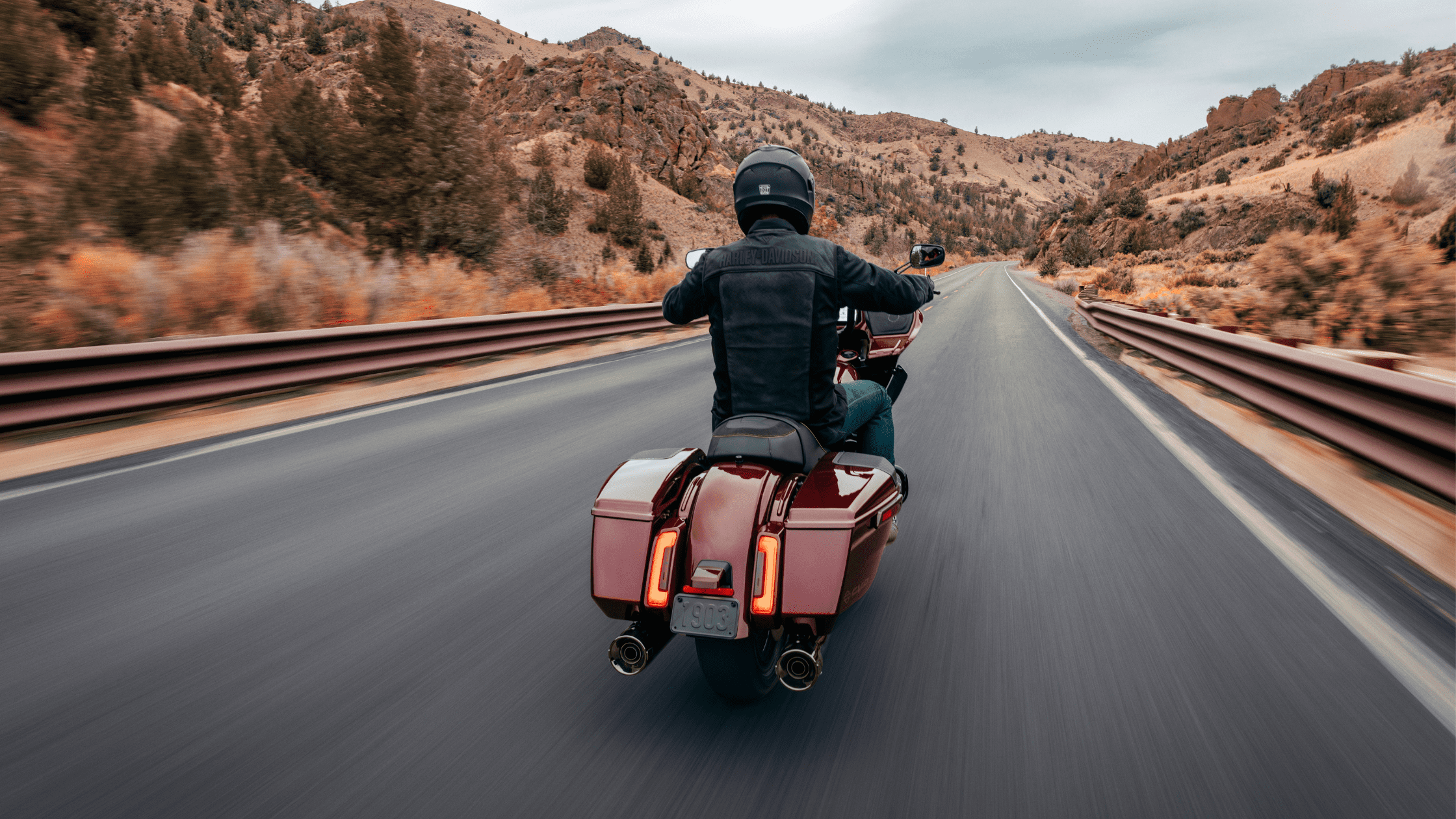 A rider wearing a helmet and riding gear drives a red Harley-Davidson CVO™ Road Glide® on a scenic mountain road, viewed from behind.