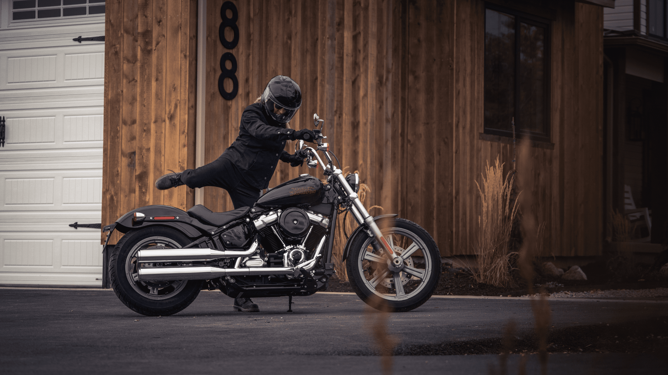Rider mounting a 2024 Softail® Standard motorcycle in front of a wooden house
