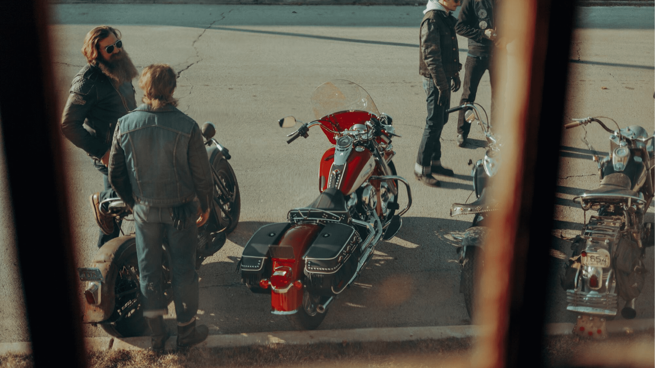 Group of motorcyclists gathered around a Harley-Davidson Hydra-Glide Revival, viewed through a window