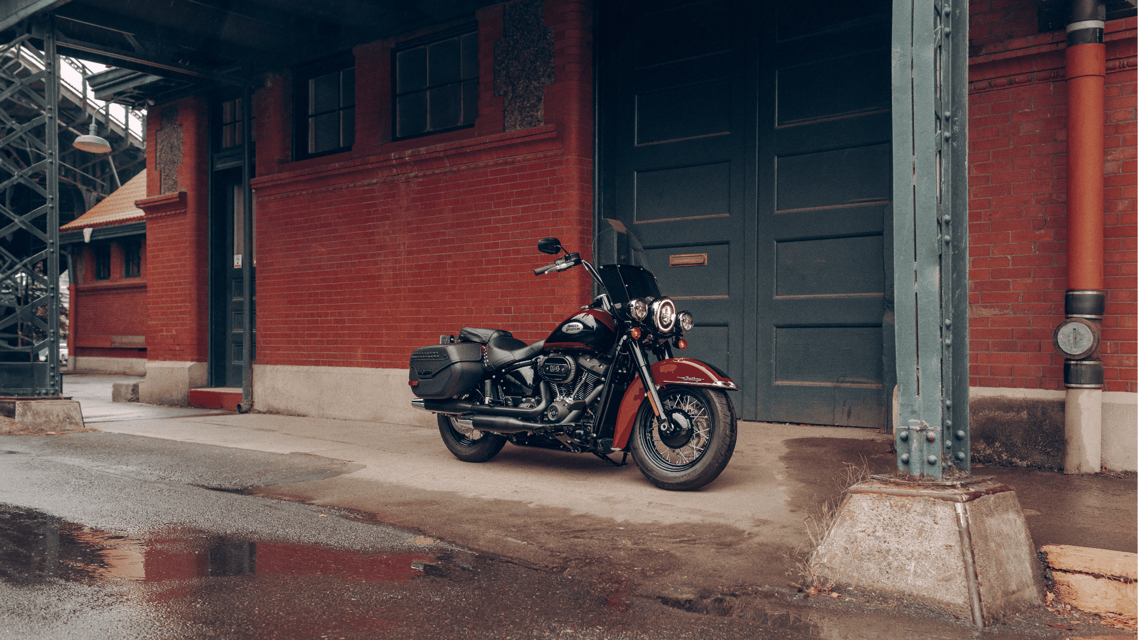 Harley-Davidson Heritage Classic 114 motorcycle parked by a brick building under a steel structure.
