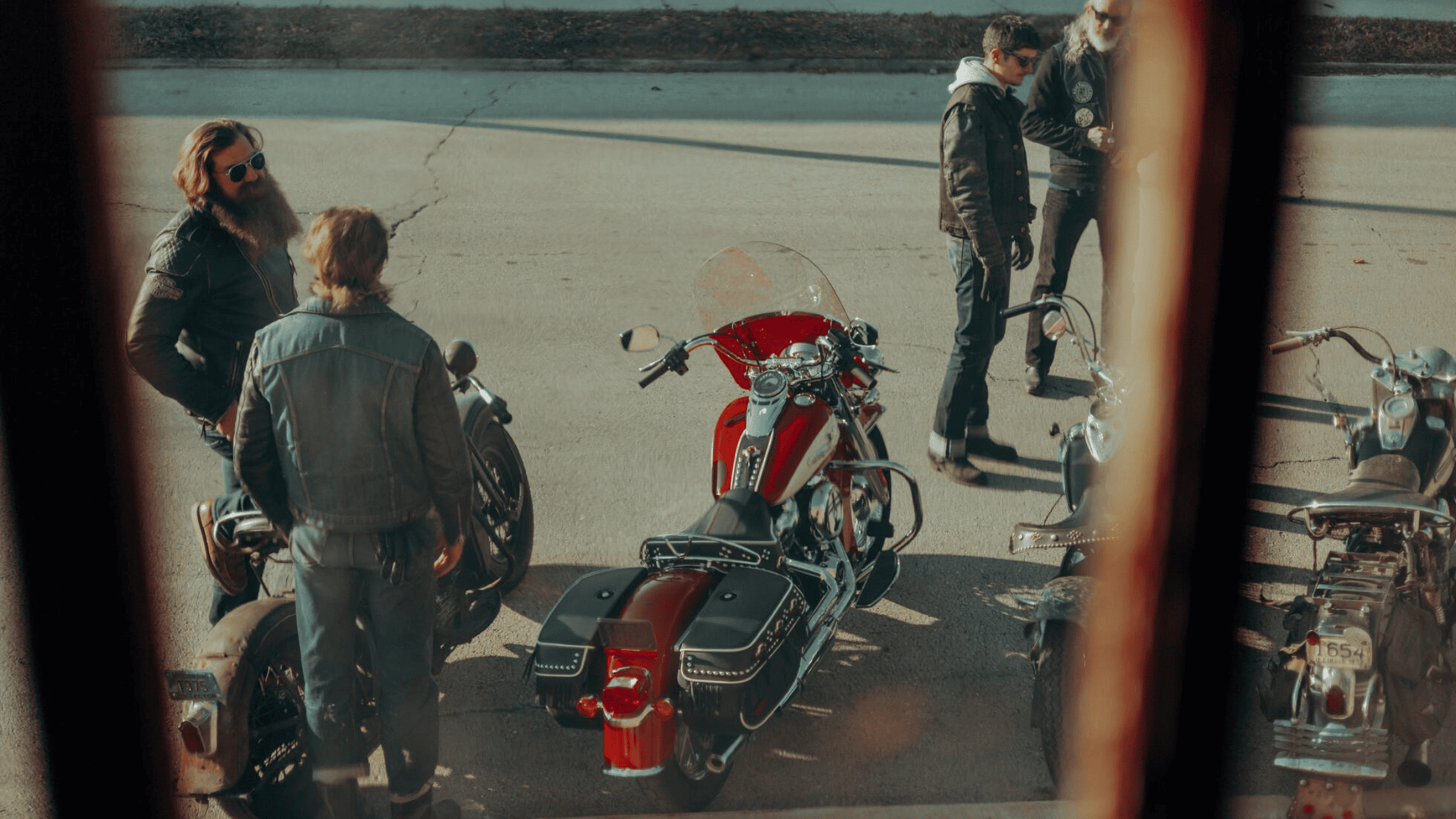 Bikers gathered around vintage motorcycles, having a conversation on the street.