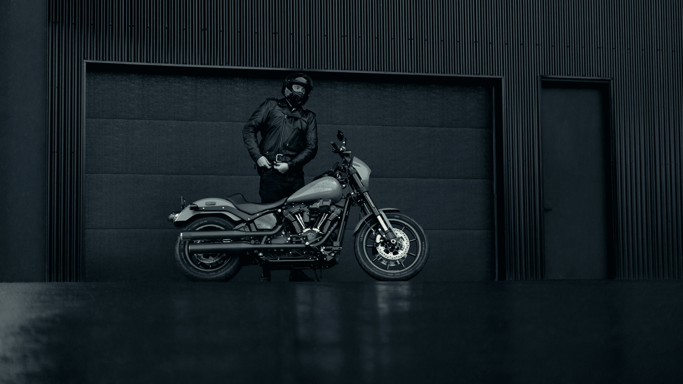 A rider stands next to a Harley-Davidson® Low Rider® S motorcycle in a minimalist, monochrome setting.
