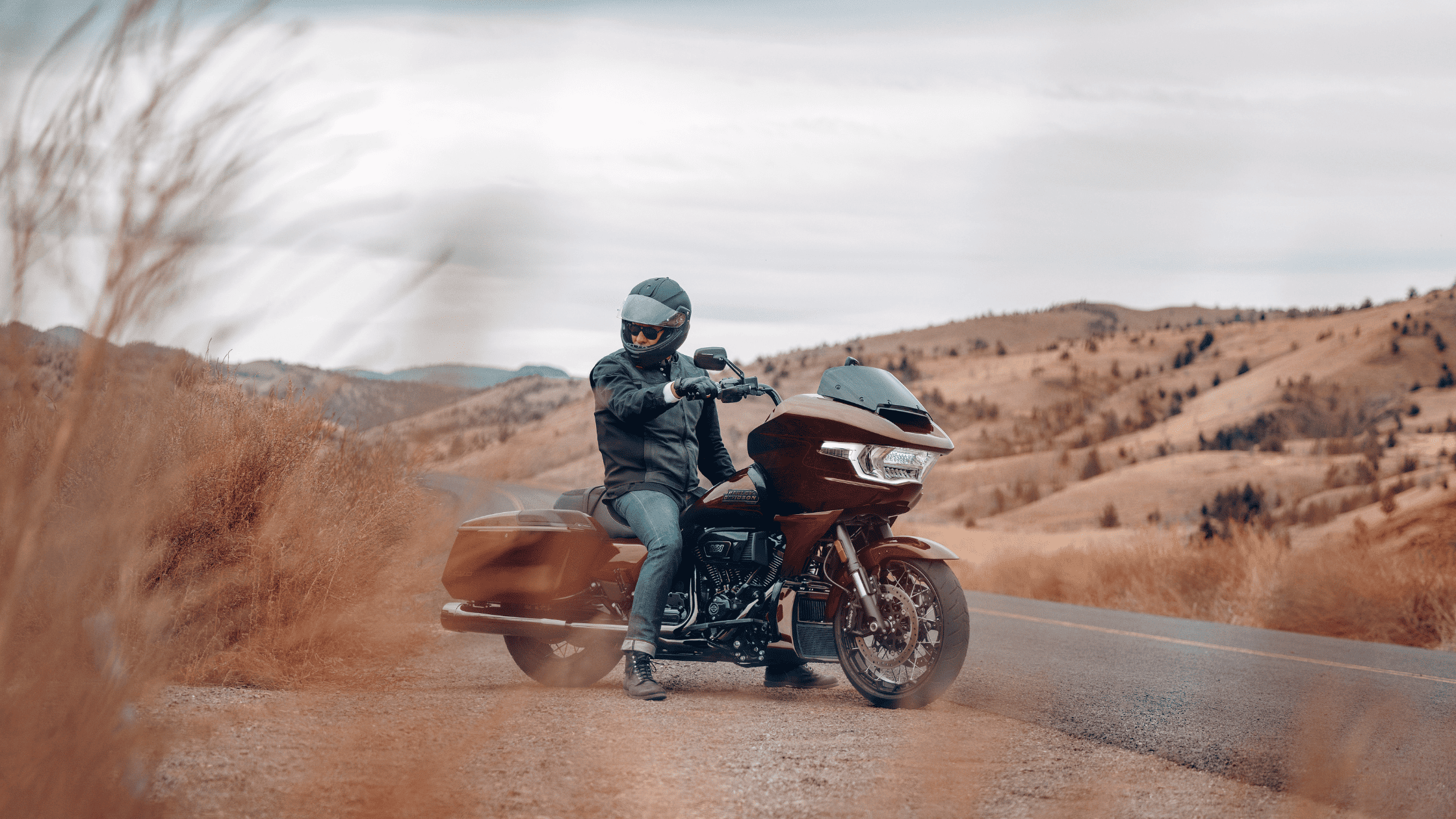 A motorcyclist wearing a helmet rides a 2024 Harley-Davidson® CVO™ Road Glide® on a scenic road surrounded by dry, hilly terrain.