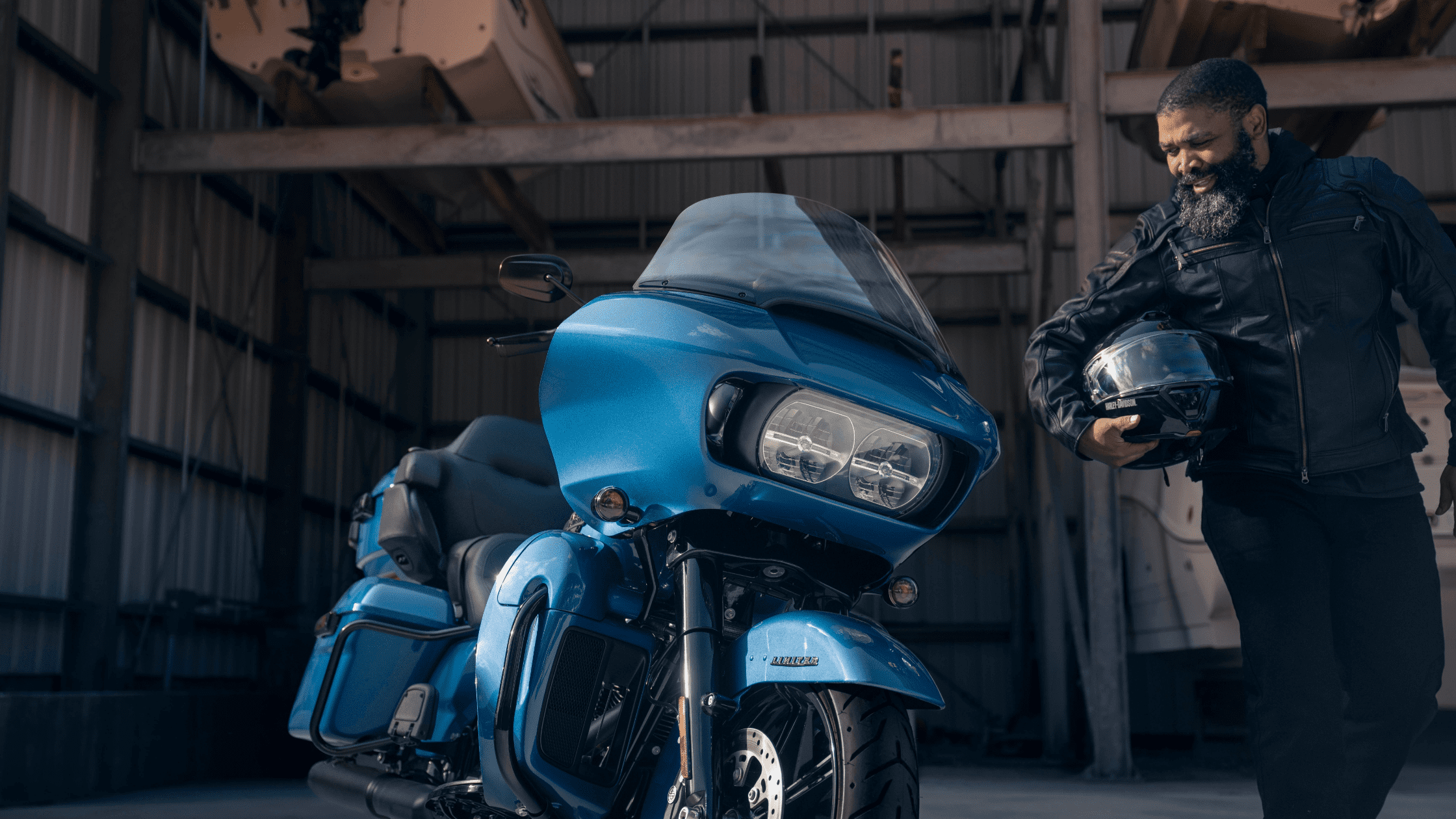 A rider standing beside a blue 2024 Harley-Davidson® Road Glide® Limited inside a garage, holding a helmet.