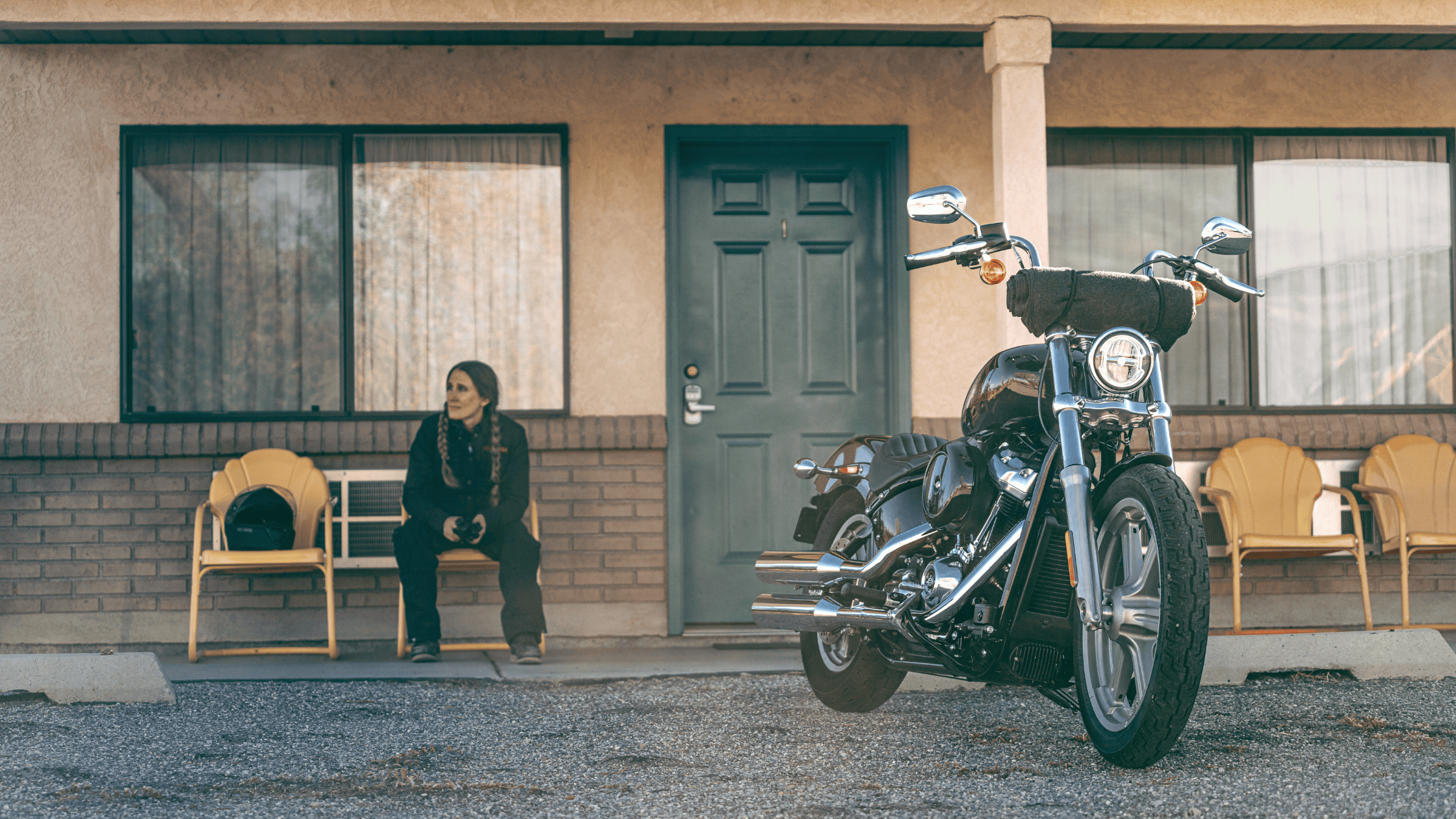 A person sits outside a motel room next to a parked 2024 Harley-Davidson® Softail® Standard motorcycle.