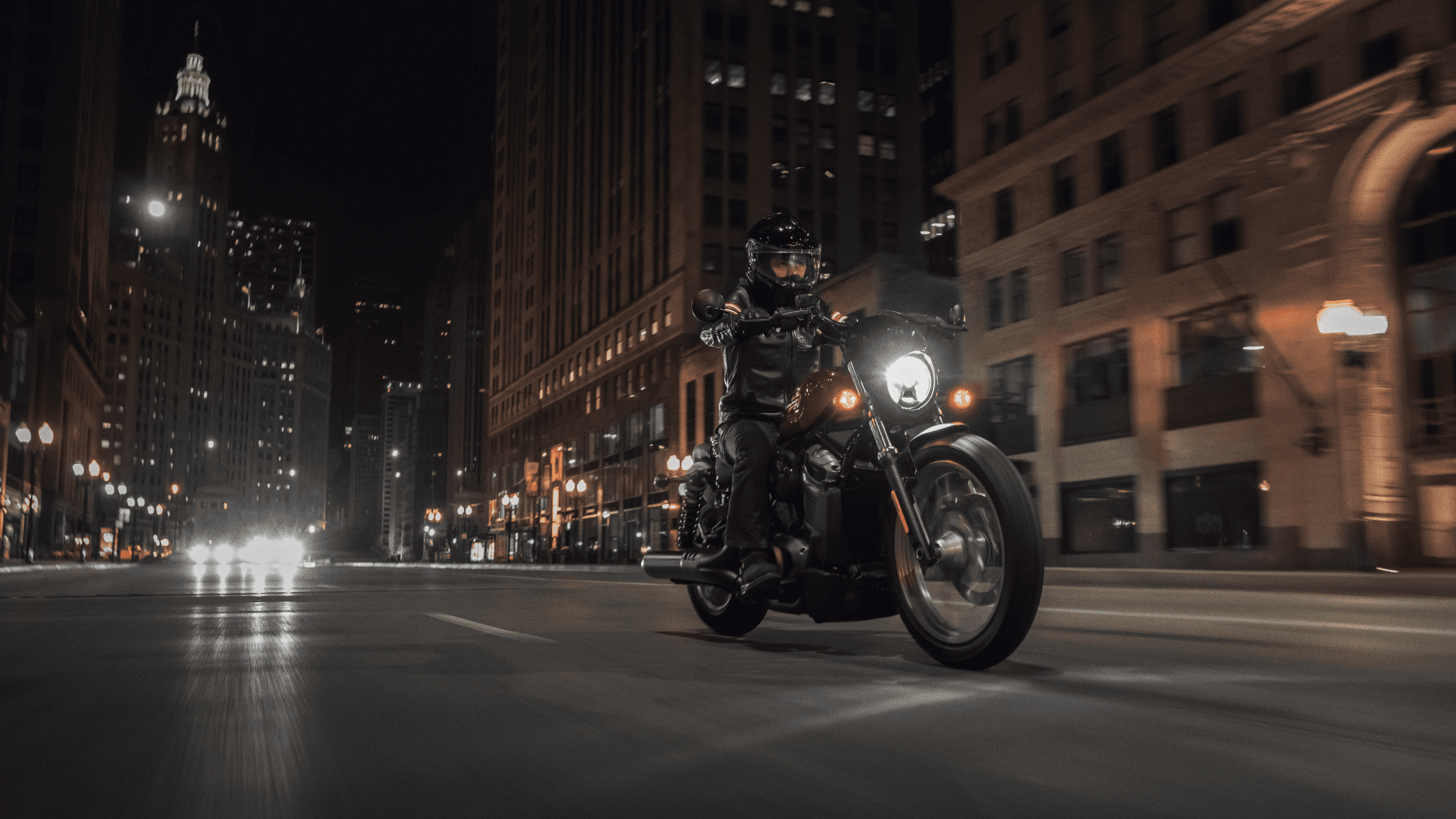 Rider on a Harley-Davidson Nightster® Special speeding through a well-lit city street at night, surrounded by tall buildings and city lights.