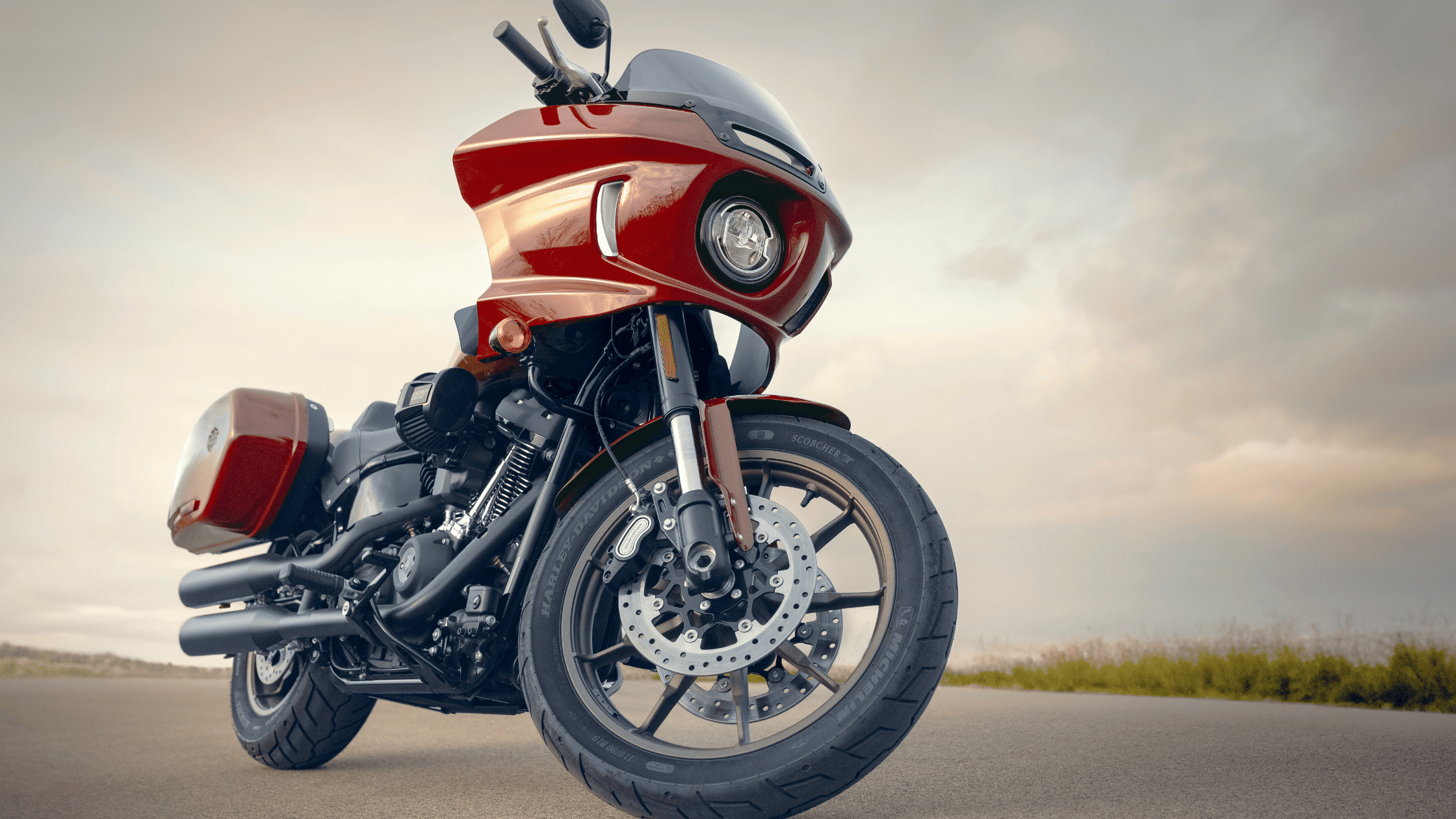 Harley-Davidson Low Rider® ST in a striking red finish, parked on an open road against a backdrop of cloudy skies.