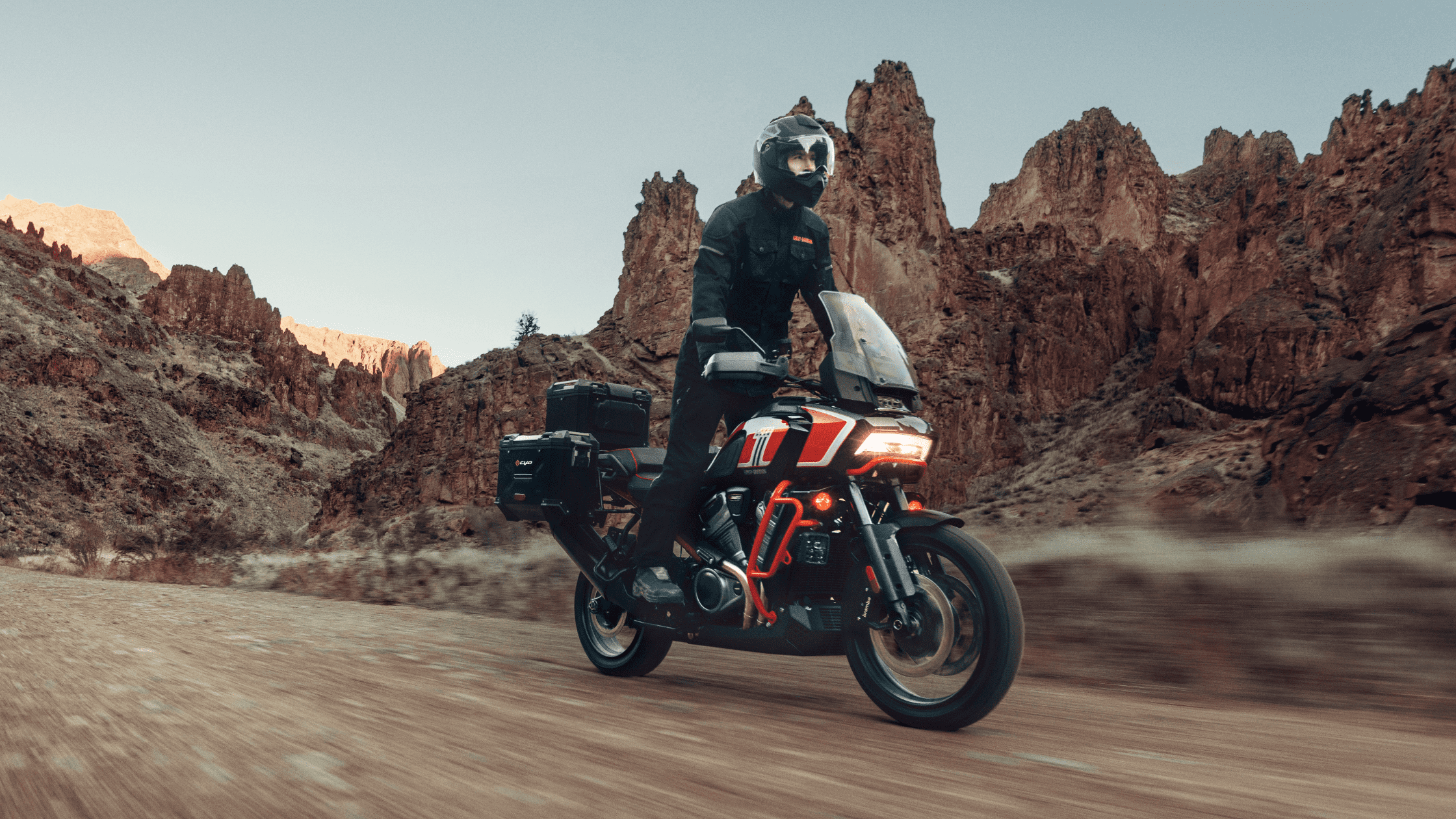 Rider on a Harley-Davidson CVO™ Pan America® adventure bike cruising through a rocky desert canyon, with rugged cliffs in the background.