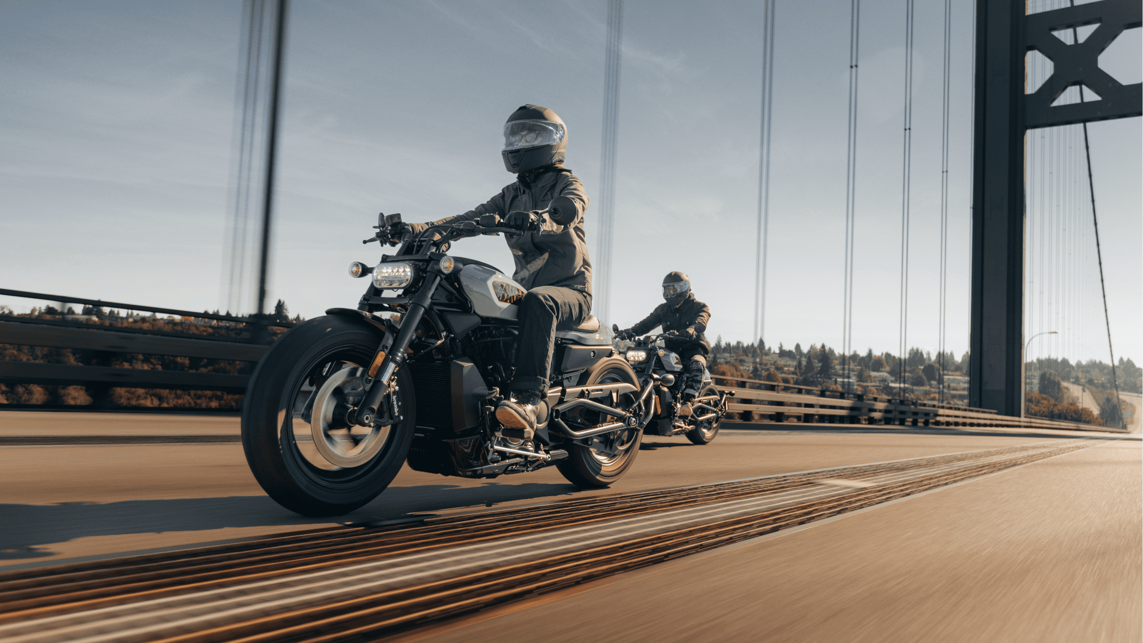 Two motorcyclists riding 2024 Harley-Davidson® Sportster® S across a bridge in Rogers, AR, on a clear day.