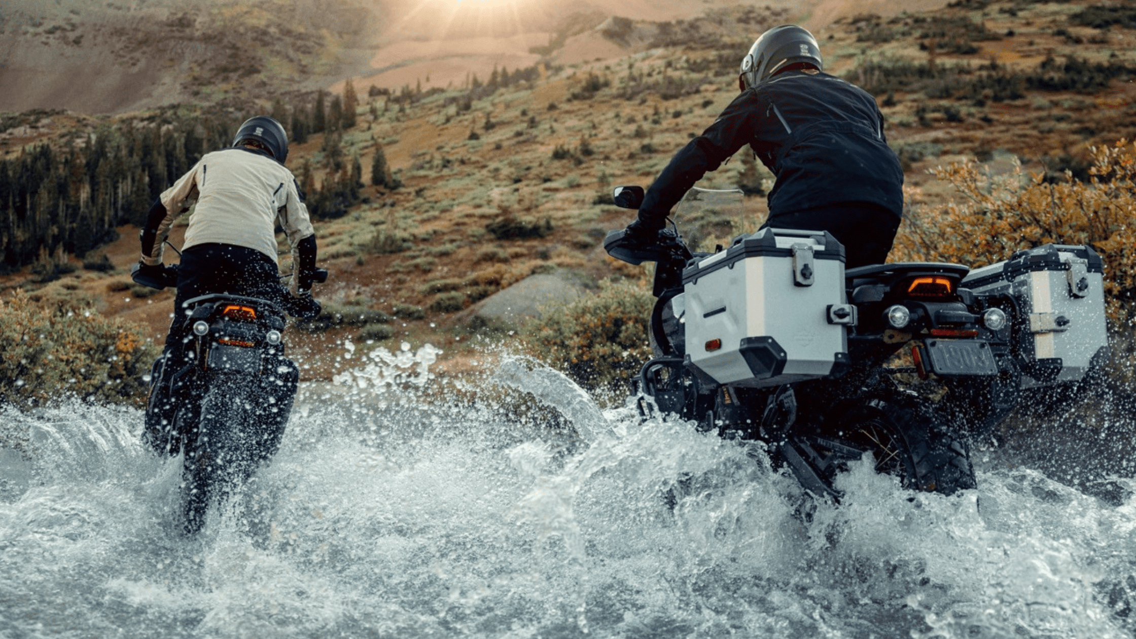 Two riders on 2024 Harley-Davidson® Pan America® 1250 Special motorcycles splash through shallow water in a mountainous landscape