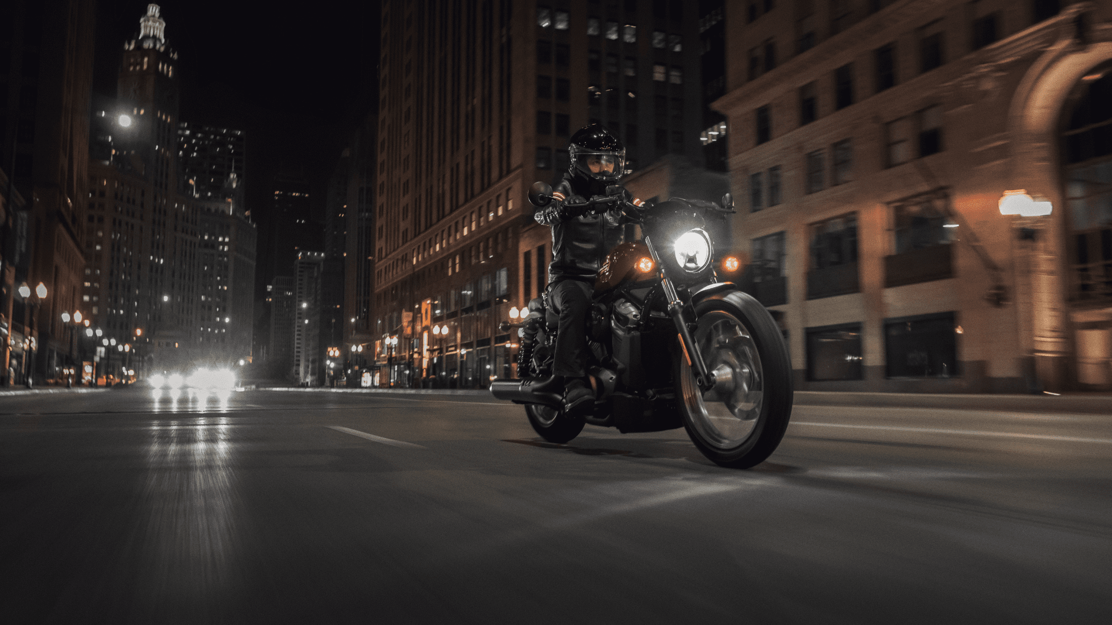 Motorcyclist riding the 2024 Harley-Davidson® Nightster® Special through downtown Rogers, AR at night, with city lights illuminating the urban scene.