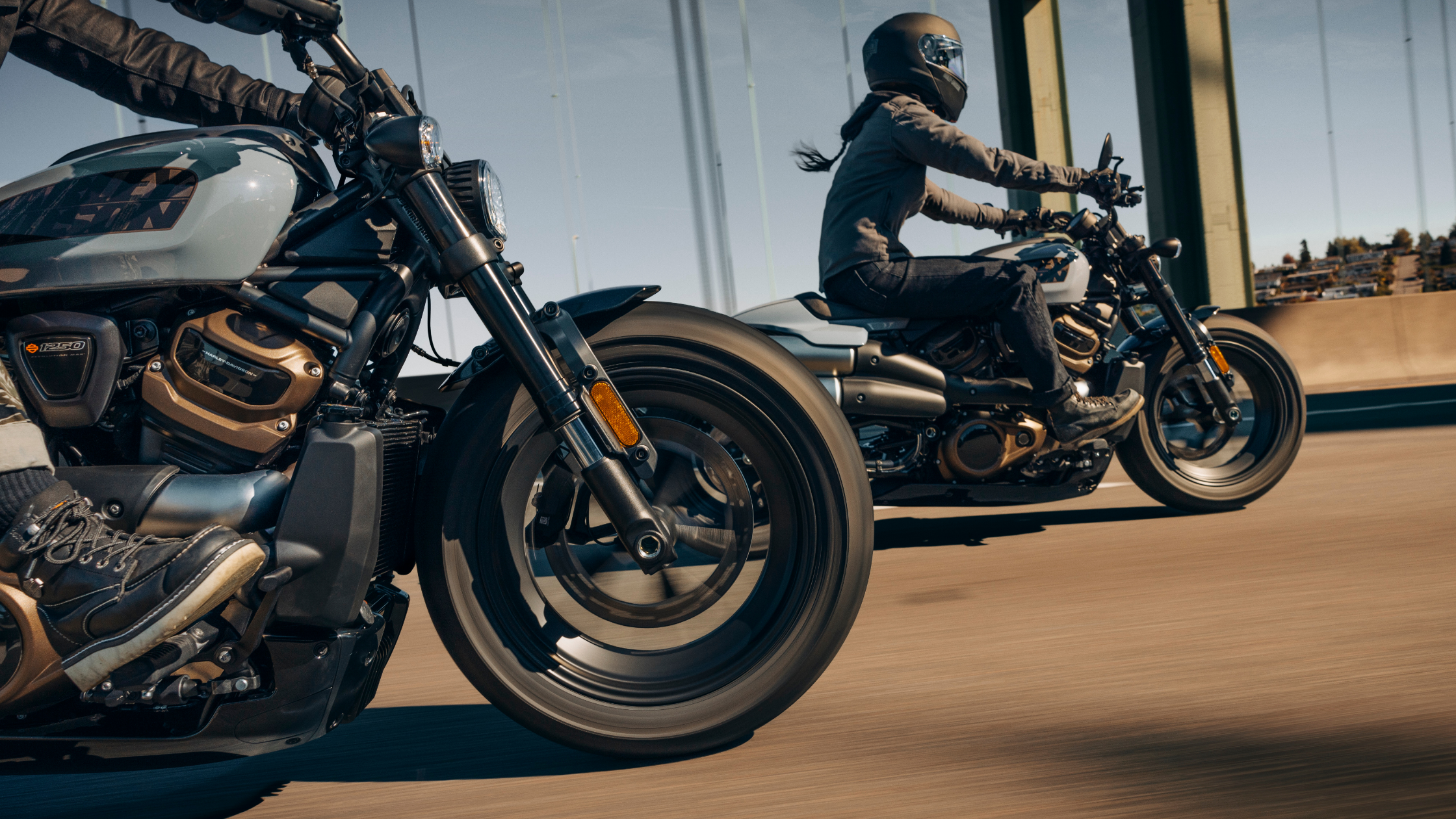 Two riders on Harley-Davidson® motorcycles cruise side by side across a bridge on a clear day.