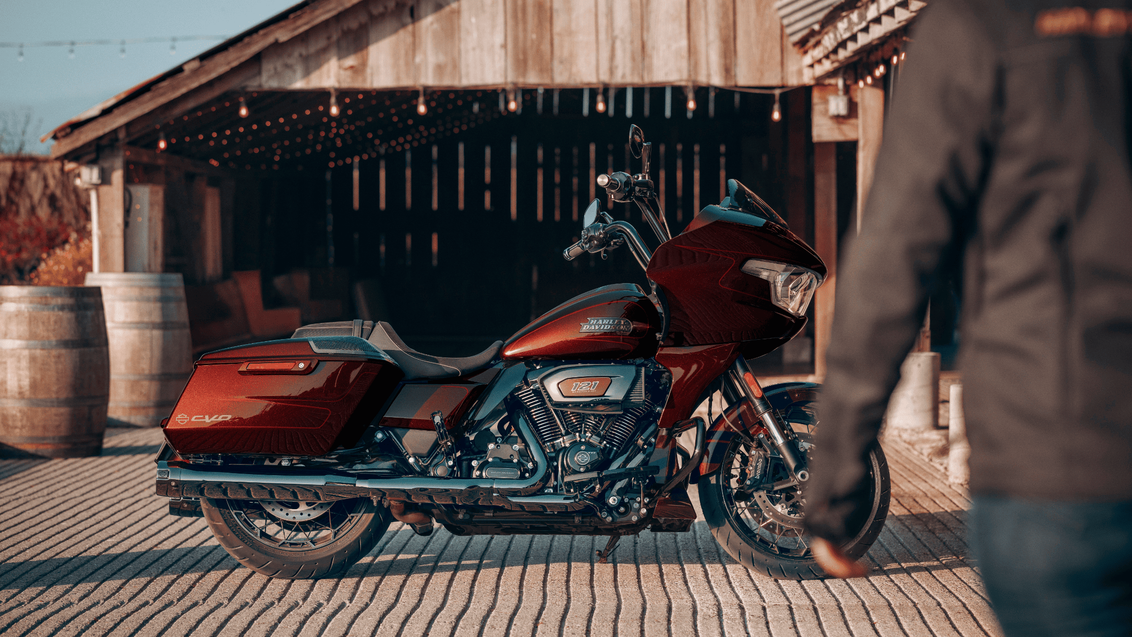 Red Harley-Davidson® CVO™ Road Glide® motorcycle parked in front of a rustic barn with a person approaching from the right.