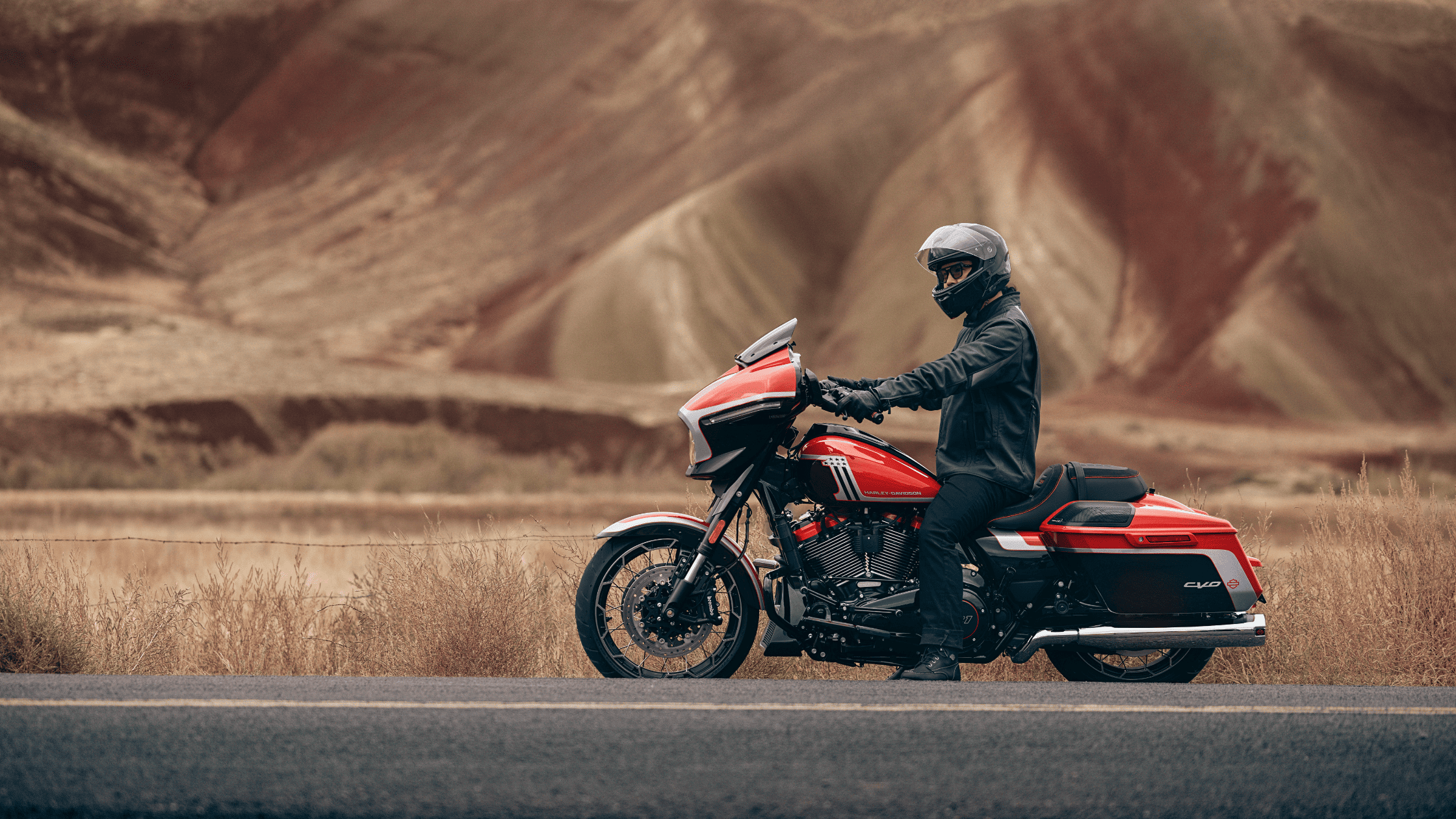Rider on a red and black Harley-Davidson® CVO™ Street Glide® motorcycle parked on a road with scenic desert mountains in the background.