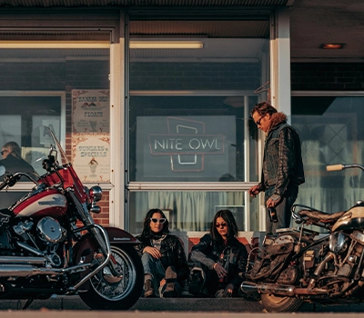 Three people socialising outside a diner with two Harley-Davidson bikes parked up