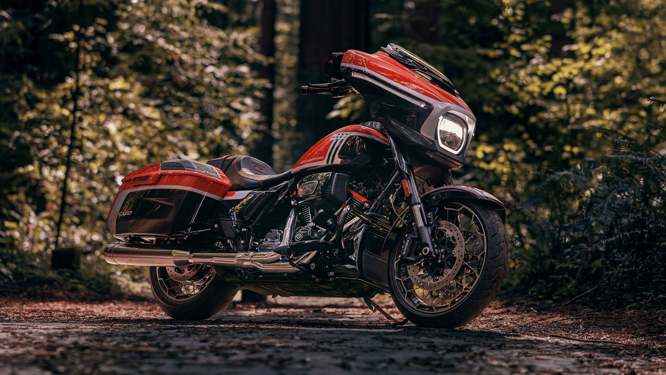 2024 Harley-Davidson CVO Street Glide in red and black, parked on a forest road surrounded by lush greenery.