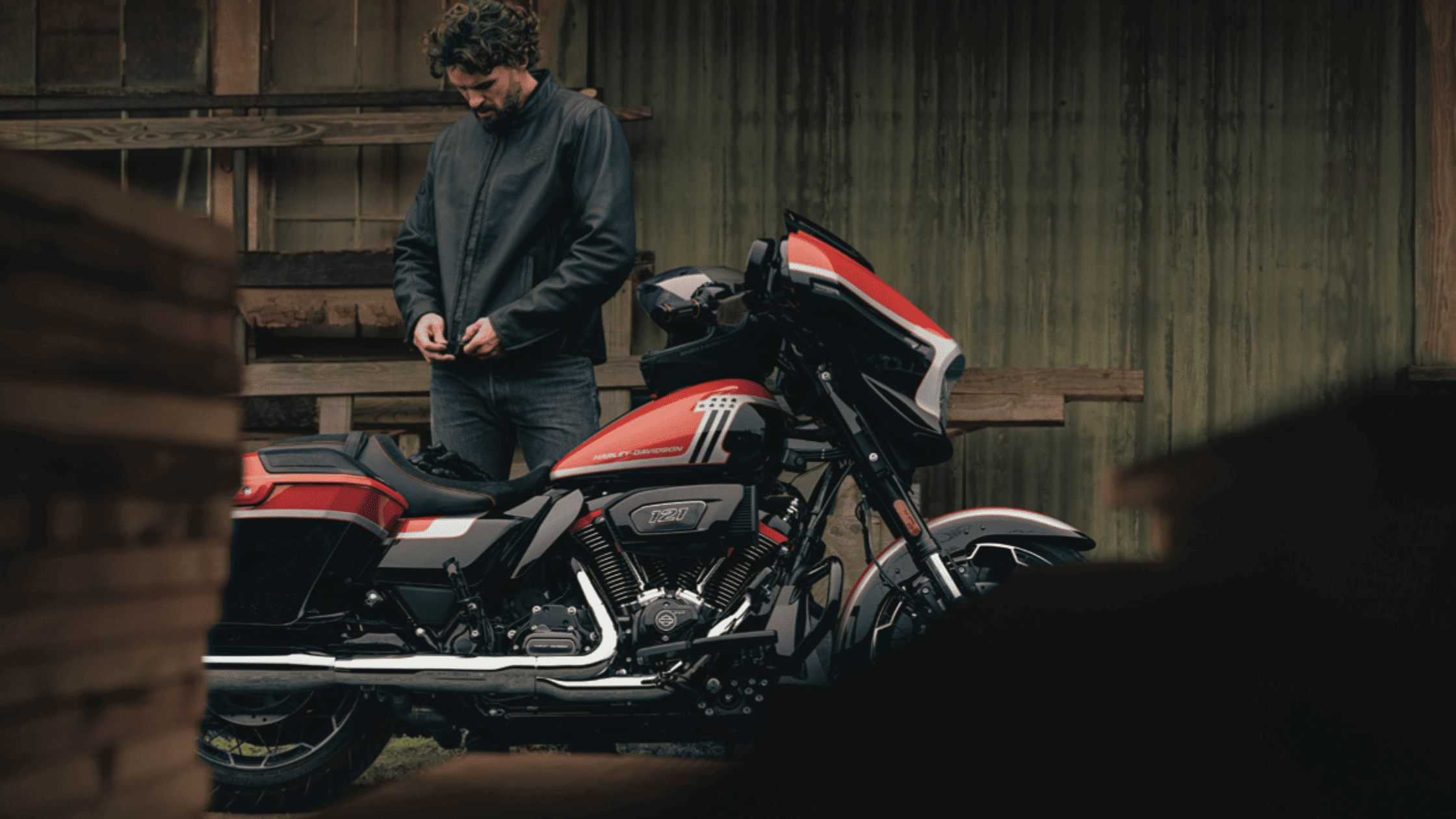 Rider standing beside a 2024 Harley-Davidson CVO Street Glide, featuring a custom red and black paint job, parked in front of a rustic building.
