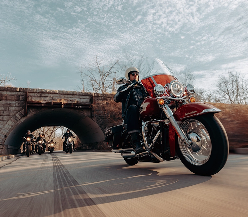 A group of motorbike riders riding harley-davidsons under a bridge
