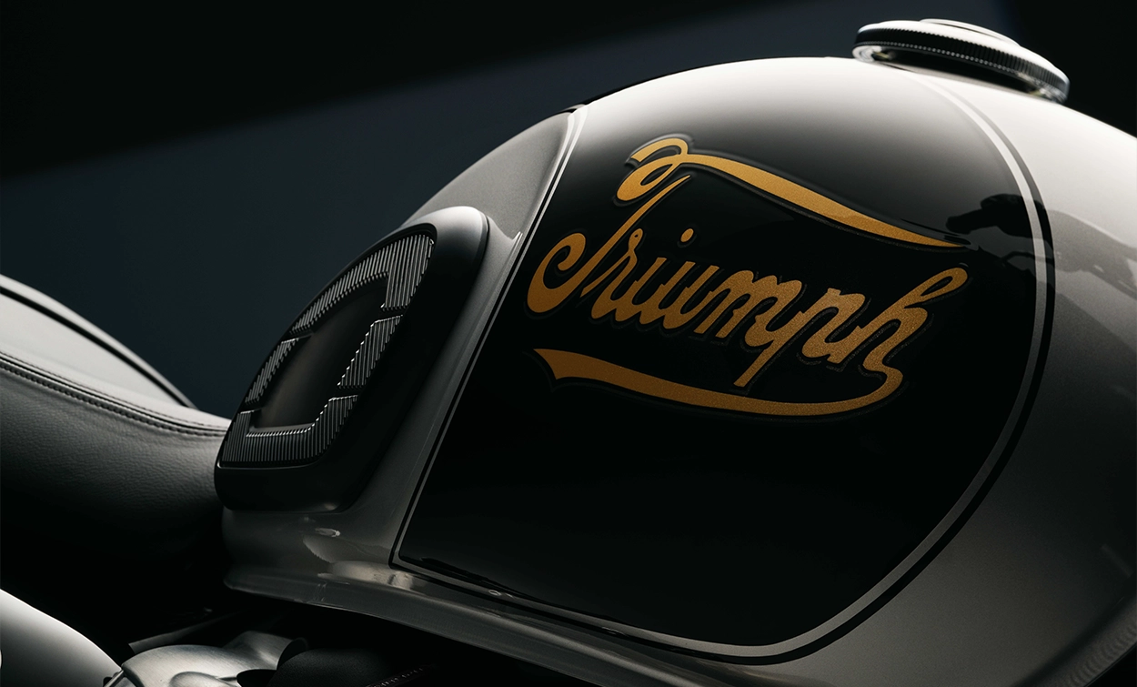A close up side shot of a black Triumph fuel tank featuring the Triumph gold script logo
