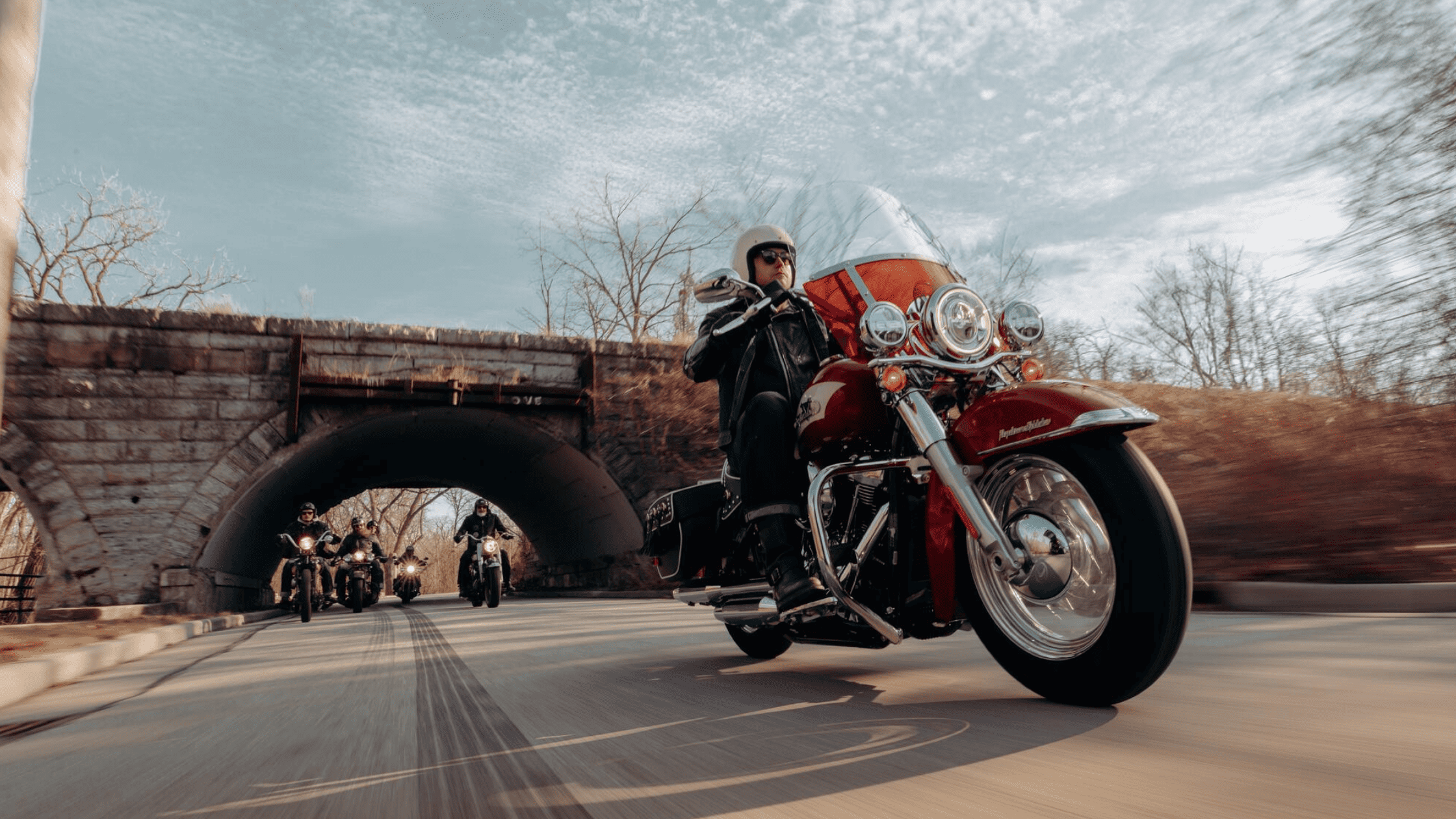 2024 Harley-Davidson® Hydra-Glide Revival leading group ride under stone bridge.