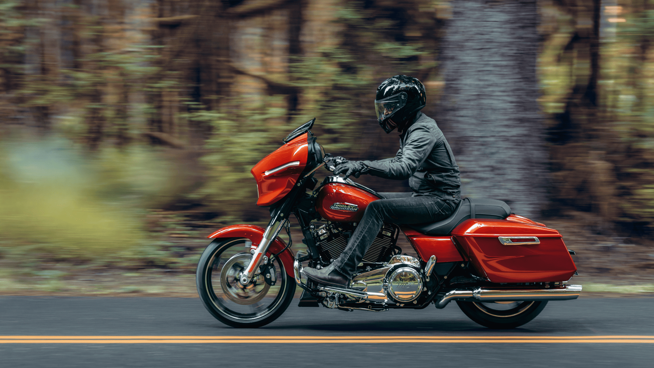 Rider cruising on a vibrant red Harley-Davidson Street Glide® through a forest.