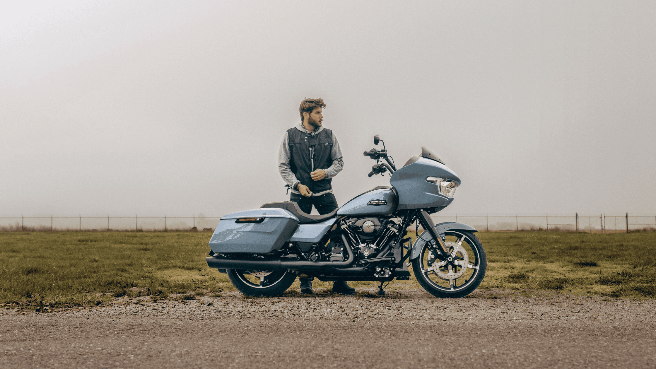 Man standing beside a sleek blue Harley-Davidson Road Glide® on a foggy day.