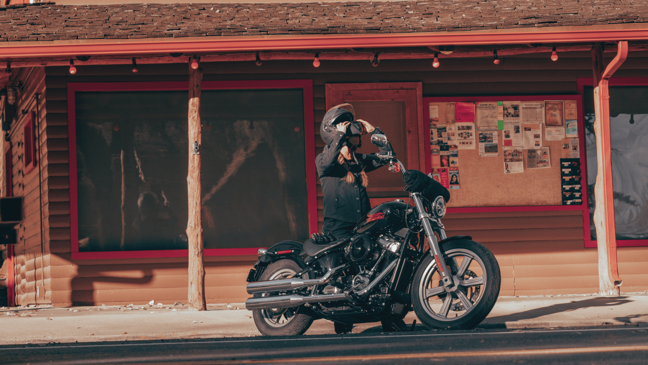 Person gearing up with a helmet next to a Harley-Davidson Softail® Standard parked in front of a rustic building.
