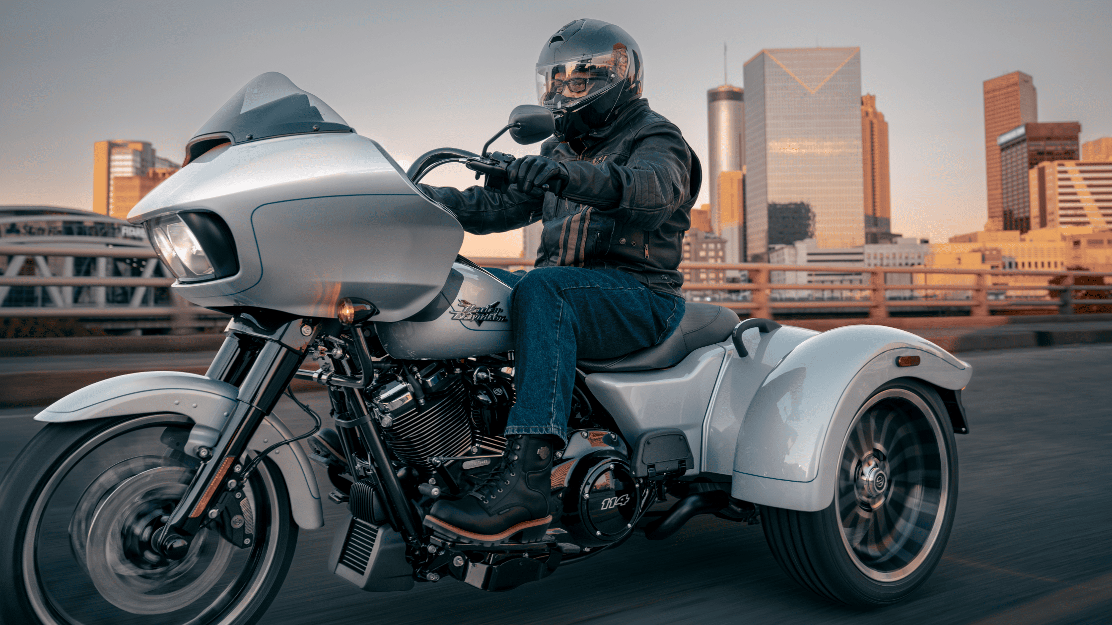 Rider on a sleek trike crossing a city bridge at sunset.