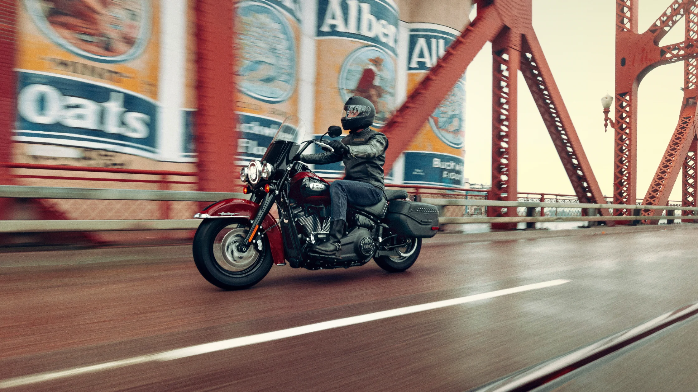 Rider on a 2024 Harley-Davidson® Heritage Classic 114 crossing a red bridge.