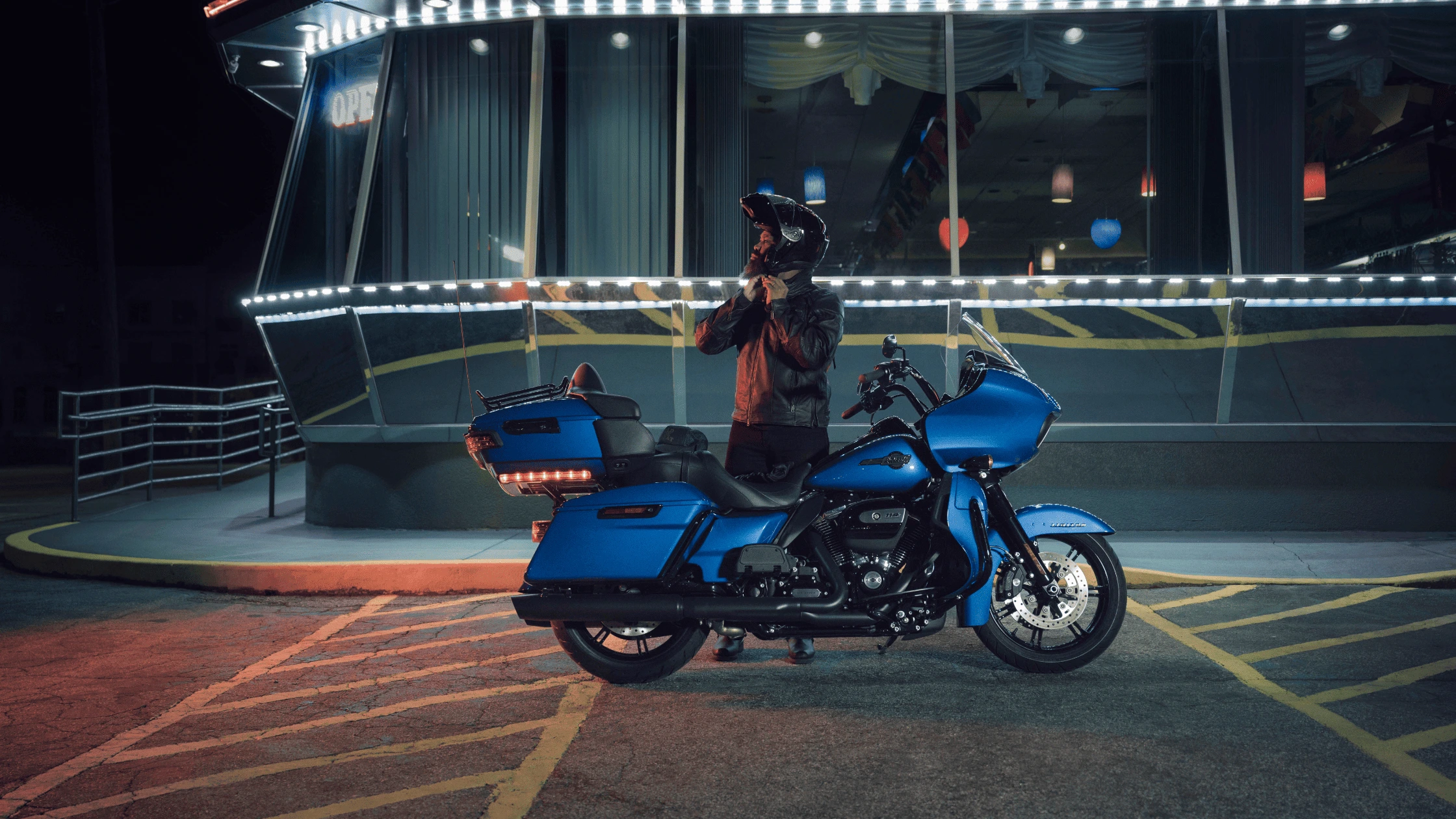 A rider with a 2024 Harley-Davidson® Road Glide® Limited near Bentonville, AR, parked in front of a neon-lit diner, showcasing the bike's luxury touring features.