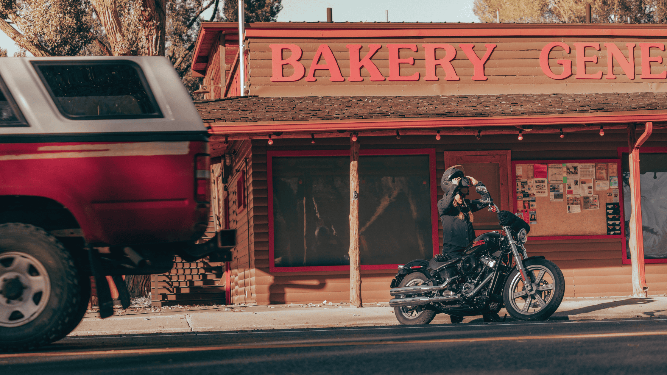 A striking red truck and a Harley Davidson Softail Standard are parked in front of a quaint bakery, enhancing the scene's appeal.