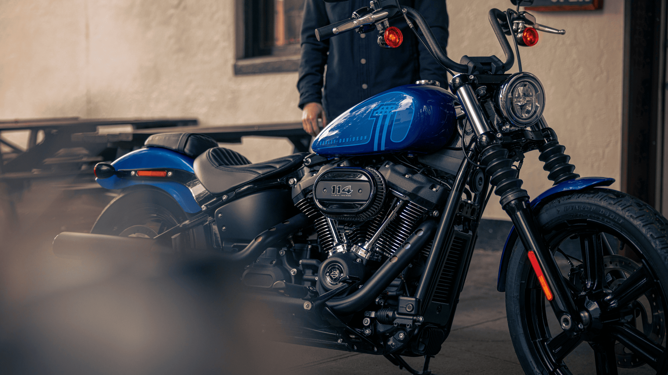 A man stands beside a blue motorcycle, smiling and enjoying the sunny day.
