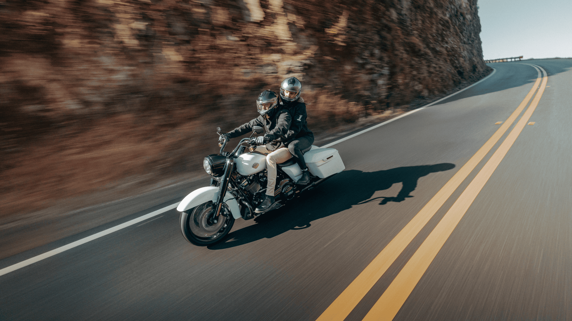A man and woman riding a motorcycle together on a scenic road, enjoying the open air and adventure.