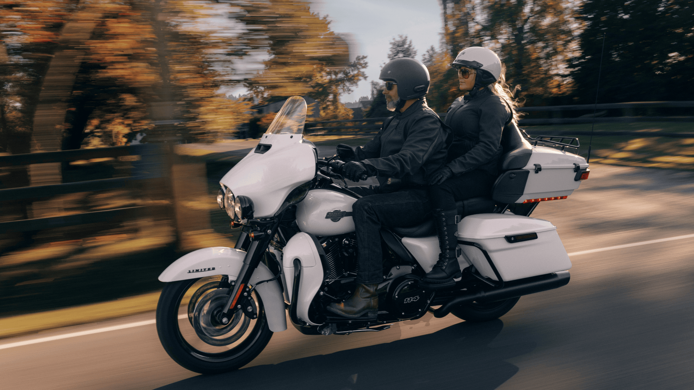 A man and woman ride a white motorcycle along a scenic road, enjoying the open air and adventure together.
