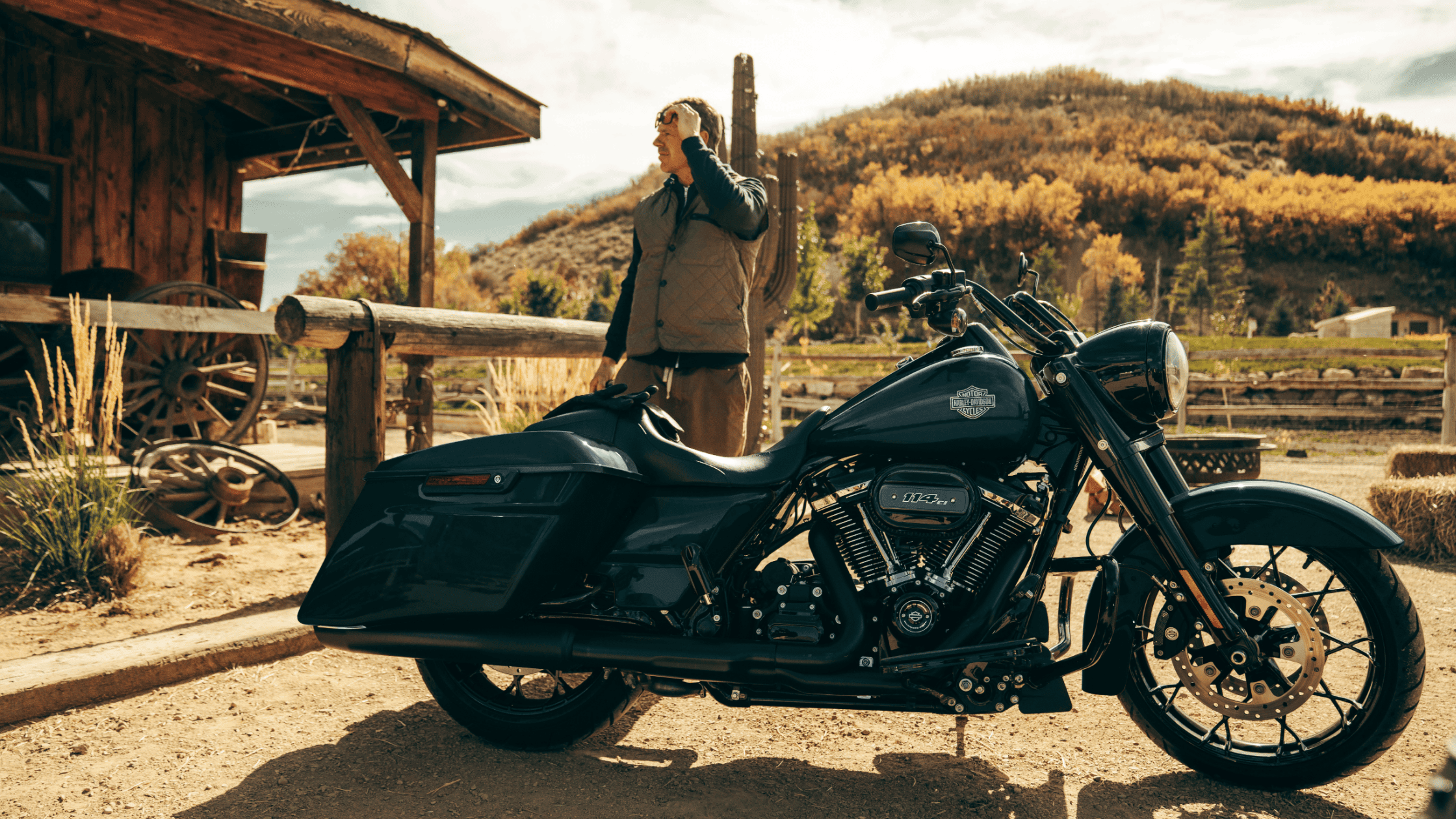 Rider standing near the 2024 Harley-Davidson® Road King® Special, parked in a rustic, countryside environment