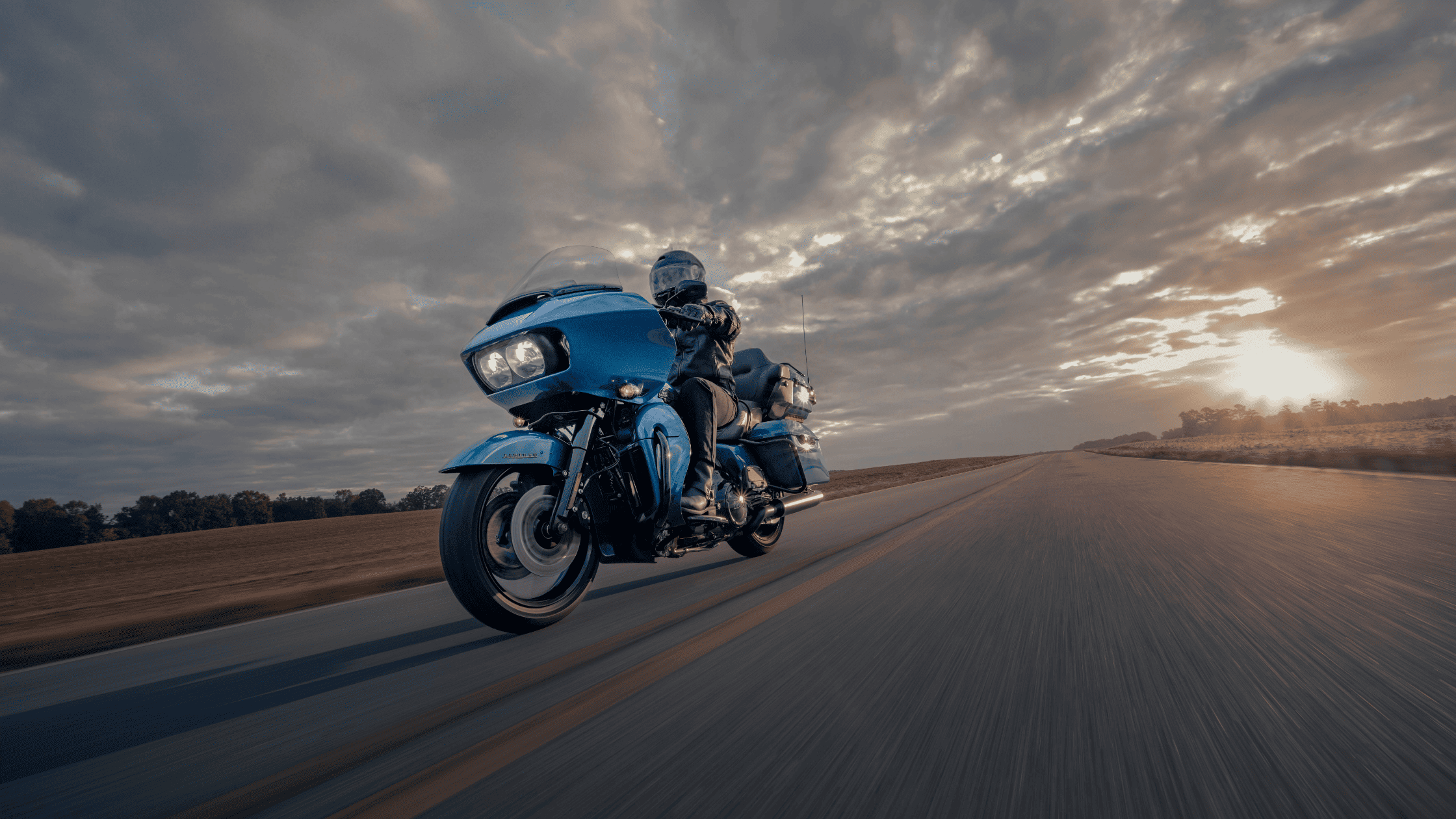 A rider on a blue Harley Davidson motorcycle travels along a winding road.