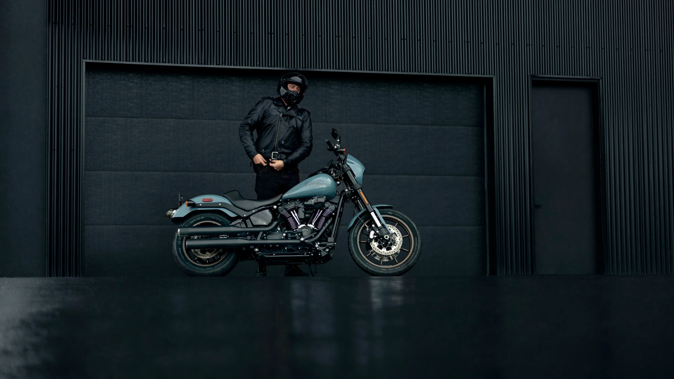 Rider standing near a Harley-Davidson Low Rider S with a sleek urban backdrop.