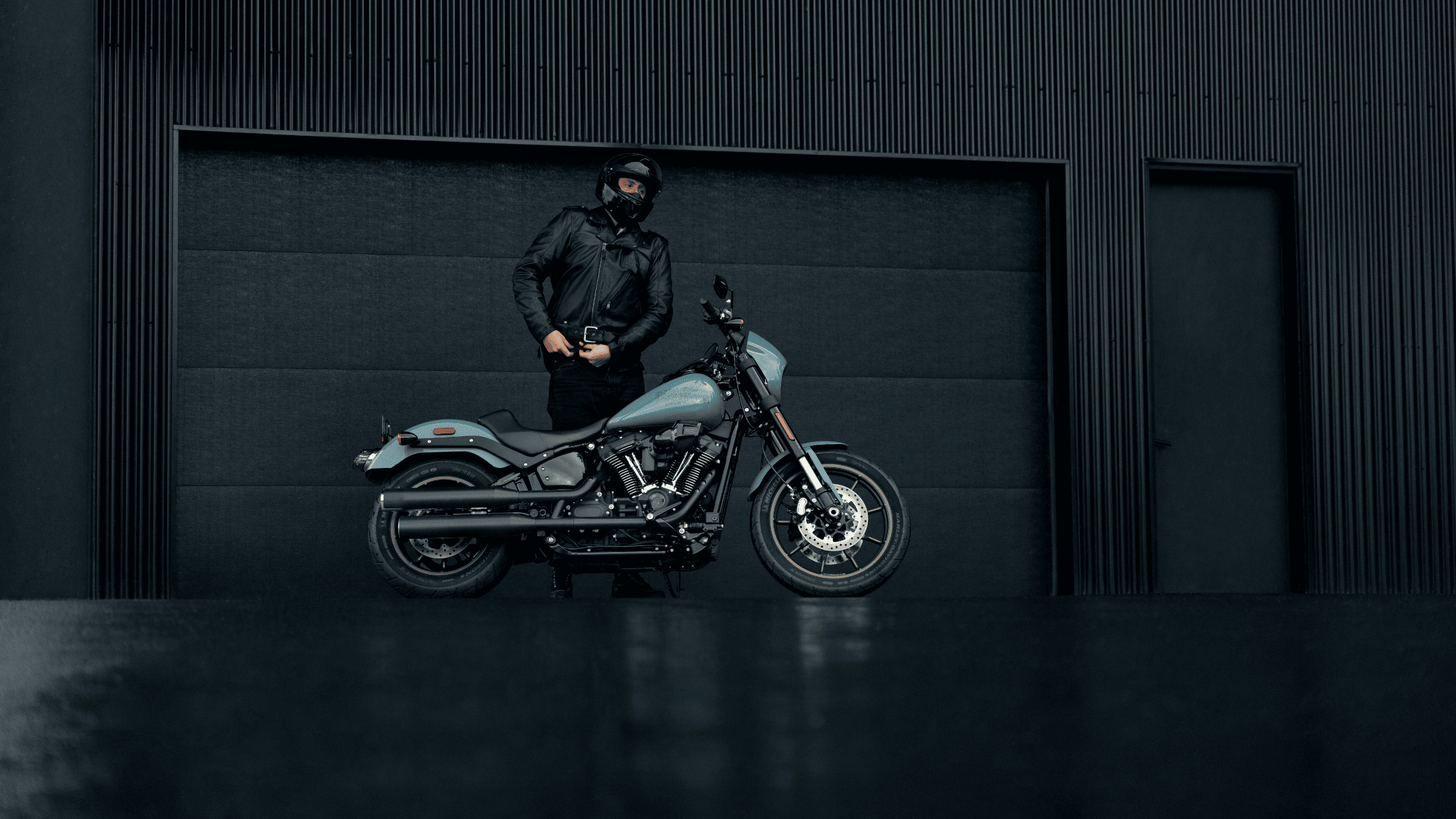 A man stands next to a Harley Davidson motorcycle in a garage, highlighting his passion for biking and motorcycle culture.