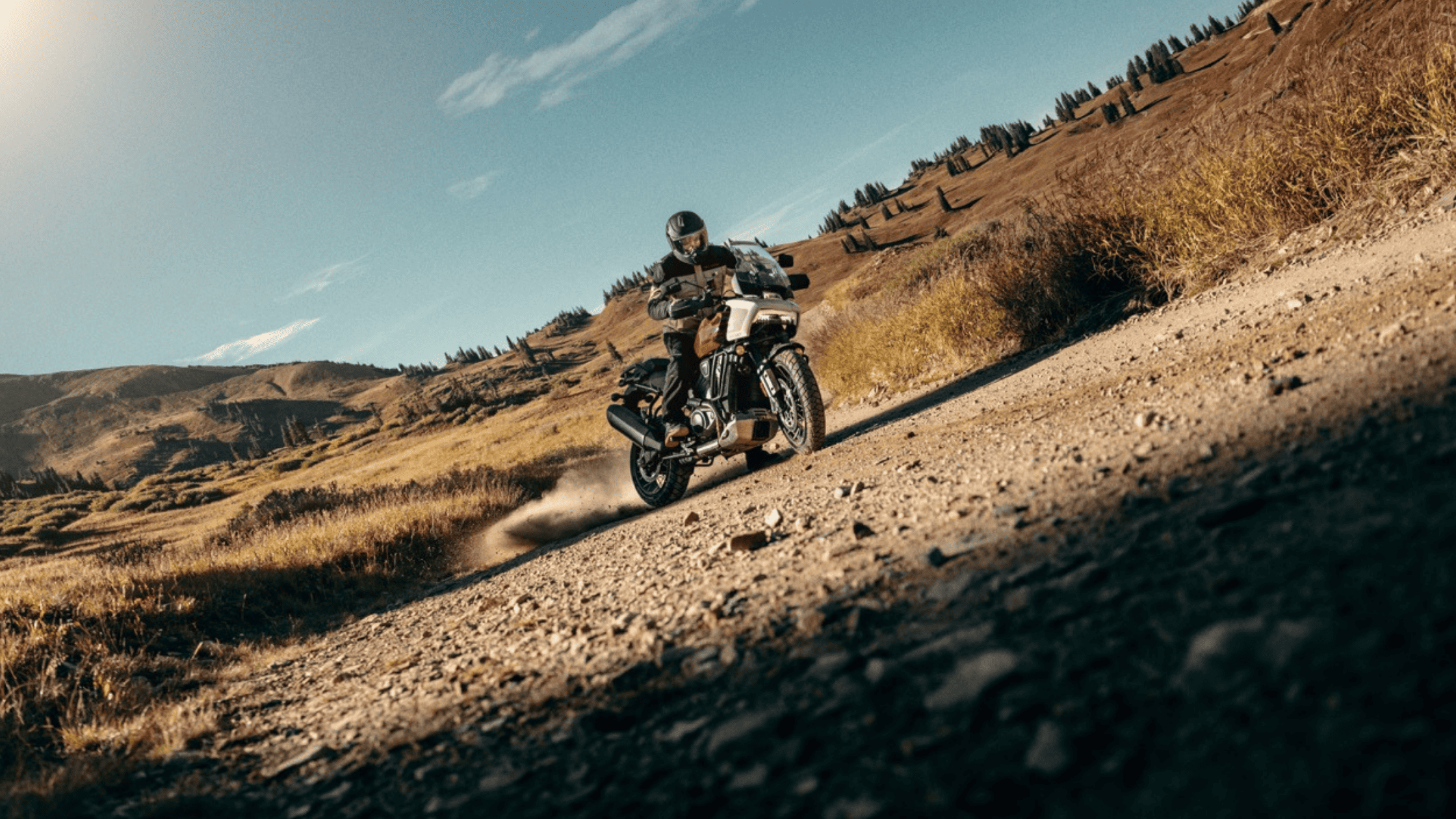 A man confidently rides a 2024 Harley-Davidson® Pan America® 1250 Special along a rugged dirt road, embracing adventure.