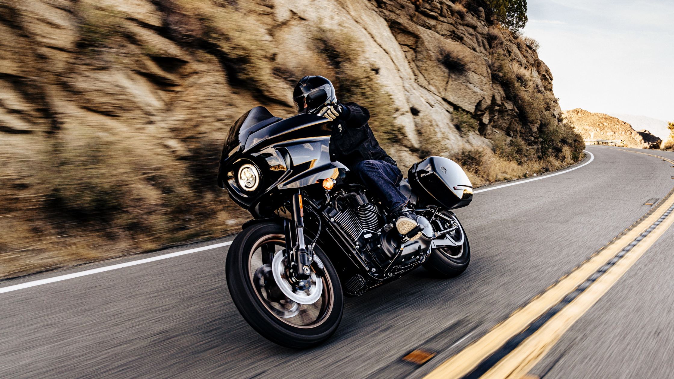 Rider on the 2024 Harley-Davidson® Low Rider® ST cruising through scenic winding roads, showcasing performance and style near Bentonville, AR.