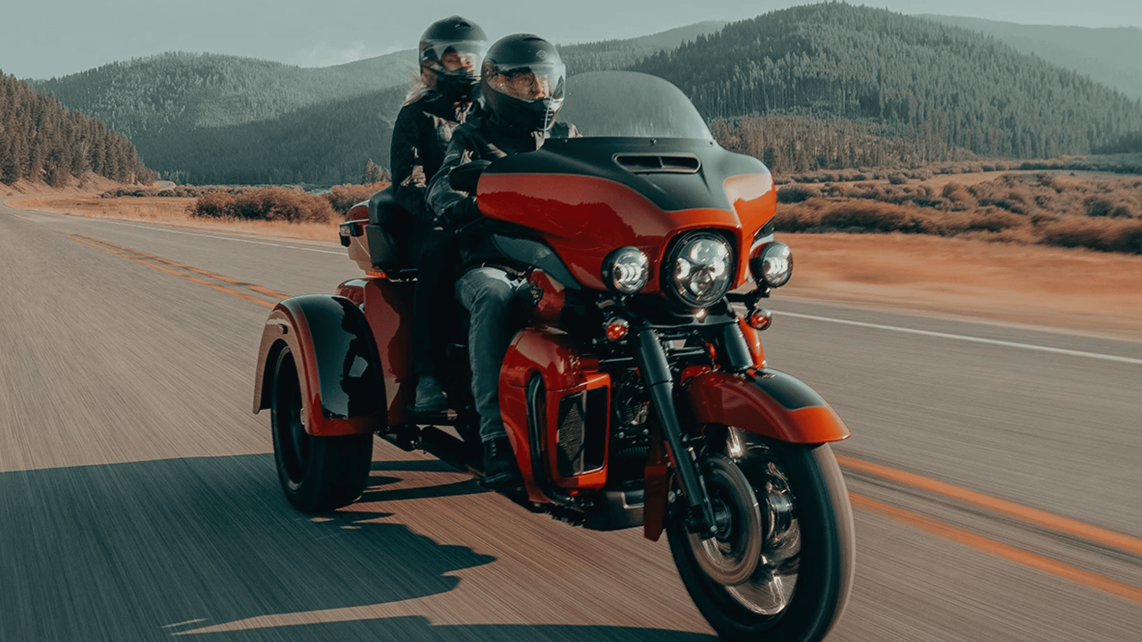Two riders enjoy a scenic road on a 2025 Harley-Davidson® Tri Glide® Ultra motorcycle, embracing the open air.